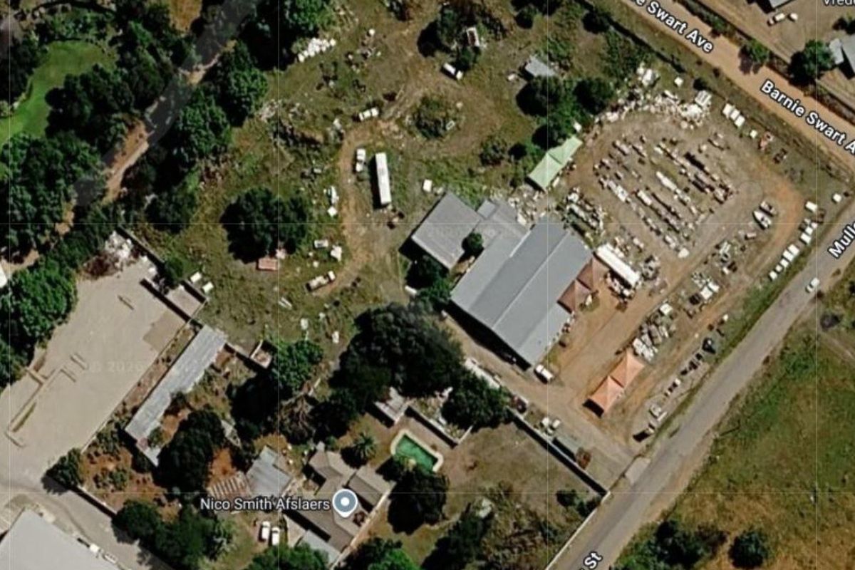 Aerial view of a commercial property featuring a warehouse, swimming pool, and extensive outdoor yard space with significant site clutter.