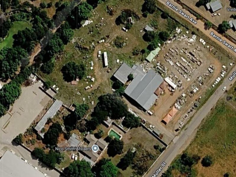 Aerial view of a commercial property featuring a warehouse, swimming pool, and extensive outdoor yard space with significant site clutter.