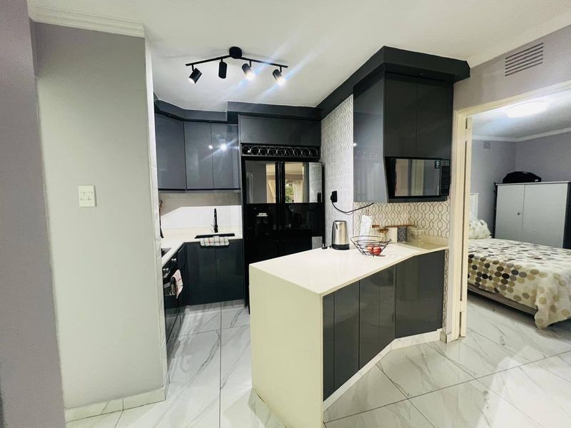 Modern kitchen featuring high-gloss cabinetry, stone countertops, integrated appliances, and stylish marble-look floor tiles with contemporary track lighting.