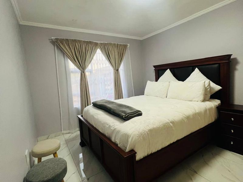 A well-maintained bedroom featuring polished marble-look floor tiles, neutral wall finishes, and a secure window with fitted security gate.