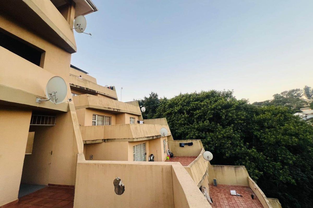 Rear view of the apartment building featuring tiered balconies with terracotta tiling and visible exterior wall wear.