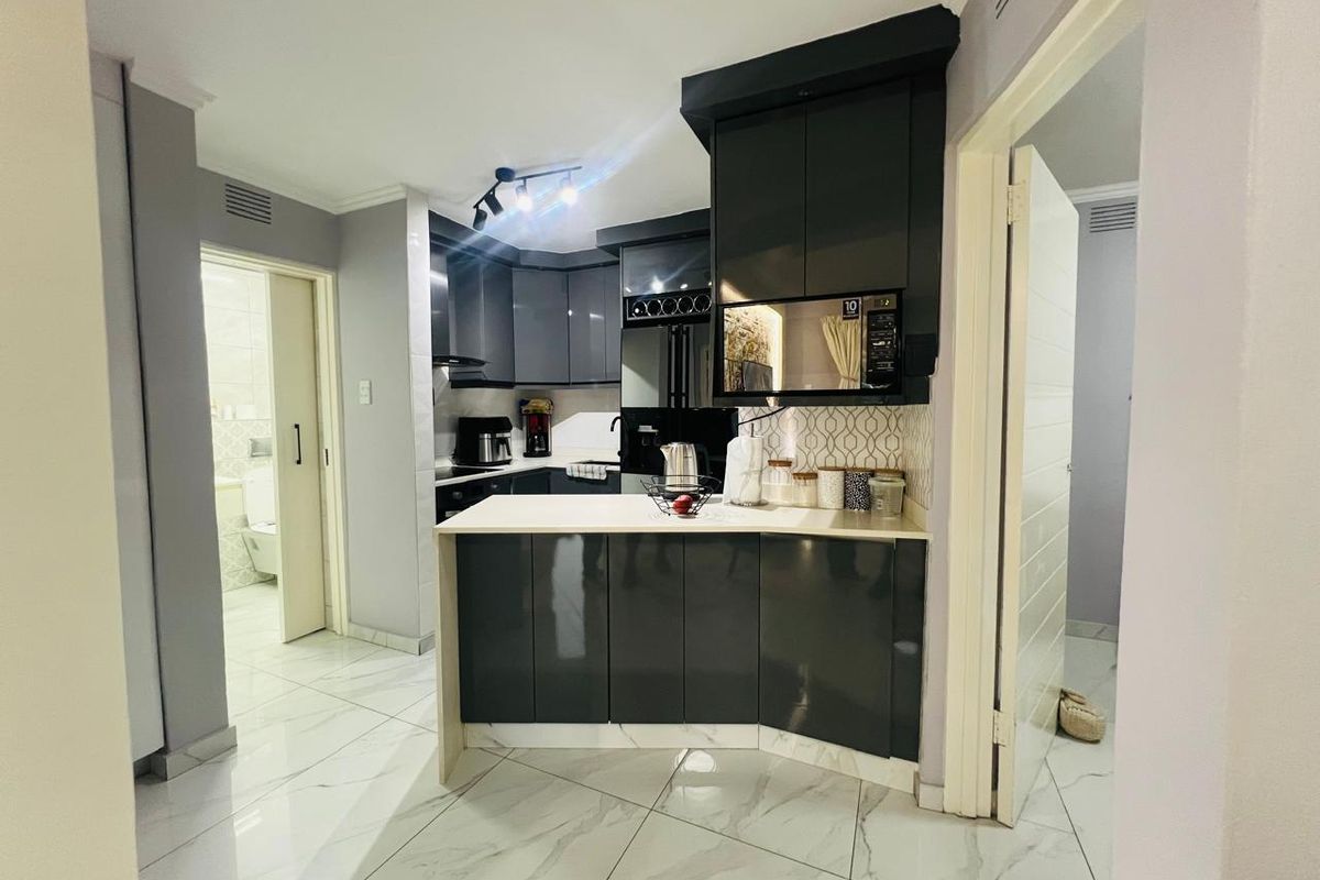 Modern kitchen featuring dark high-gloss cabinetry, stone countertops, built-in microwave, and sleek tiled flooring, offering a contemporary and functional cooking space.