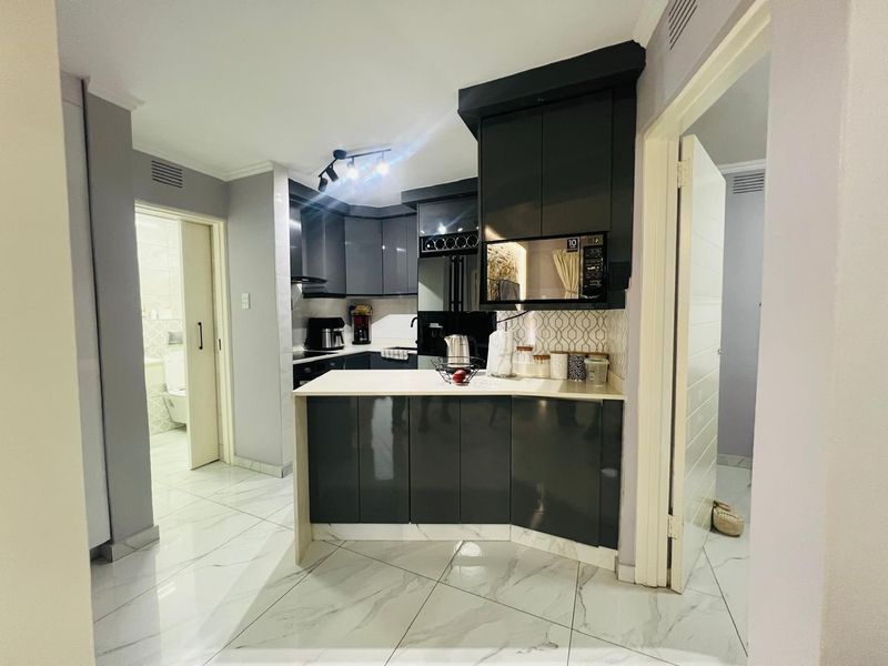 Modern kitchen featuring dark high-gloss cabinetry, stone countertops, built-in microwave, and sleek tiled flooring, offering a contemporary and functional cooking space.