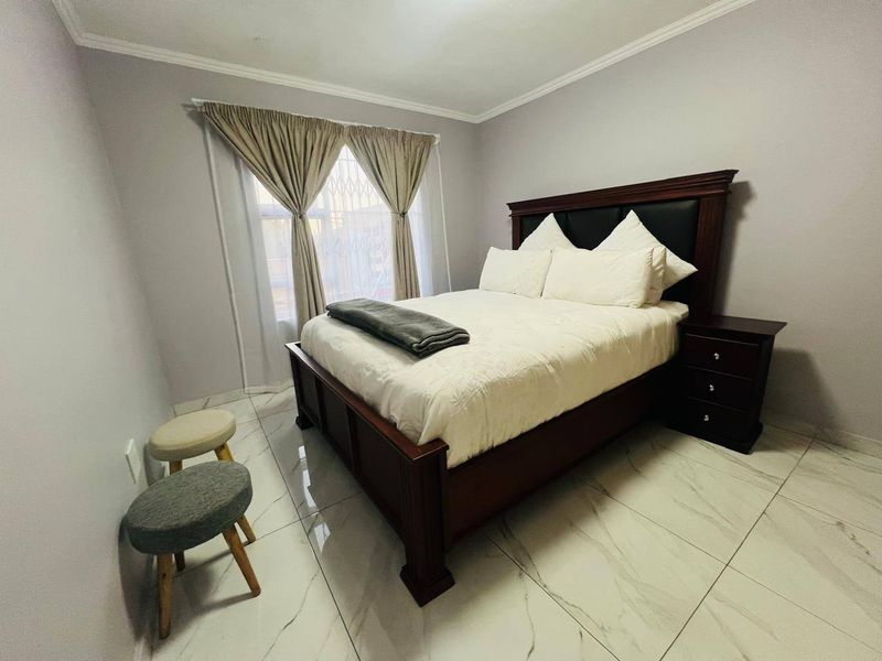 A well-maintained bedroom featuring modern marble-look tiled flooring, neutral wall finishes, and a security gate on the window.