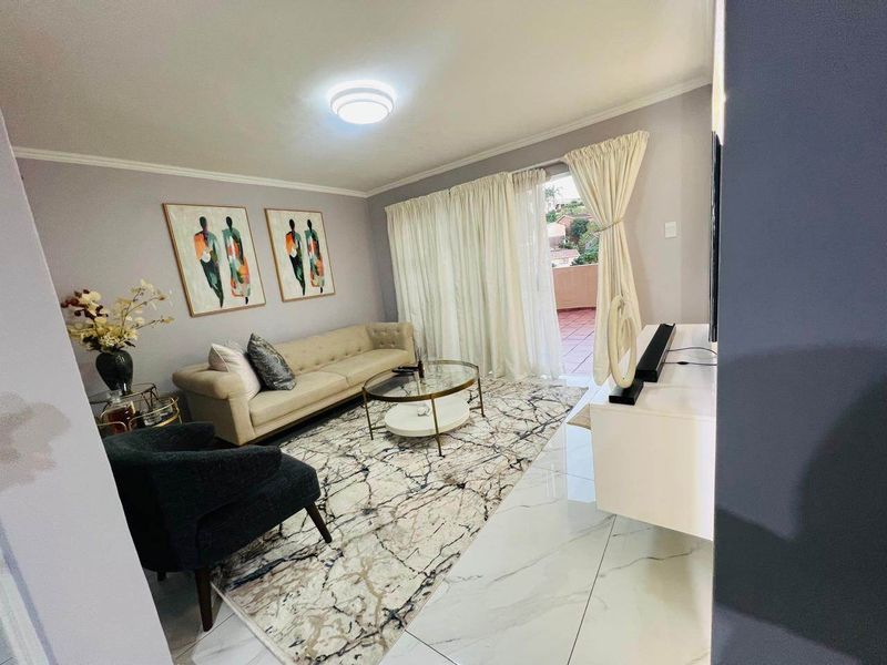 A well-maintained living room featuring polished marble-look floor tiles and a sliding glass door providing access to an outdoor balcony area.
