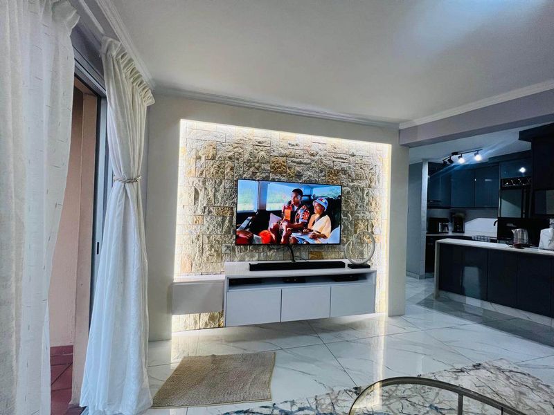 Modern open-plan living area featuring a striking stone feature wall with integrated lighting, sleek floating cabinetry, and polished marble-look flooring flowing into the kitchen.