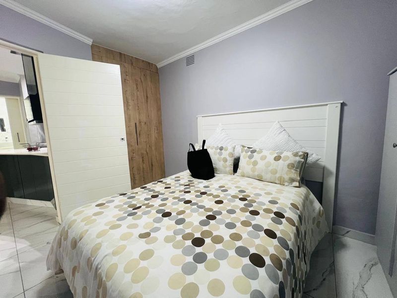 A well-maintained bedroom featuring built-in wooden cupboards, modern tiled flooring, and decorative ceiling cornicing, with an adjacent view into a bathroom area.