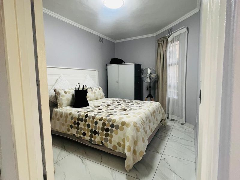 A well-maintained bedroom featuring modern marble-look floor tiles, neutral wall paint, and classic ceiling cornicing, offering a clean and bright living space.