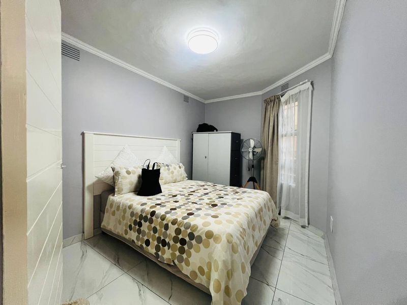 A well-maintained bedroom featuring modern marble-look floor tiles, neutral grey walls, and decorative ceiling cornicing.