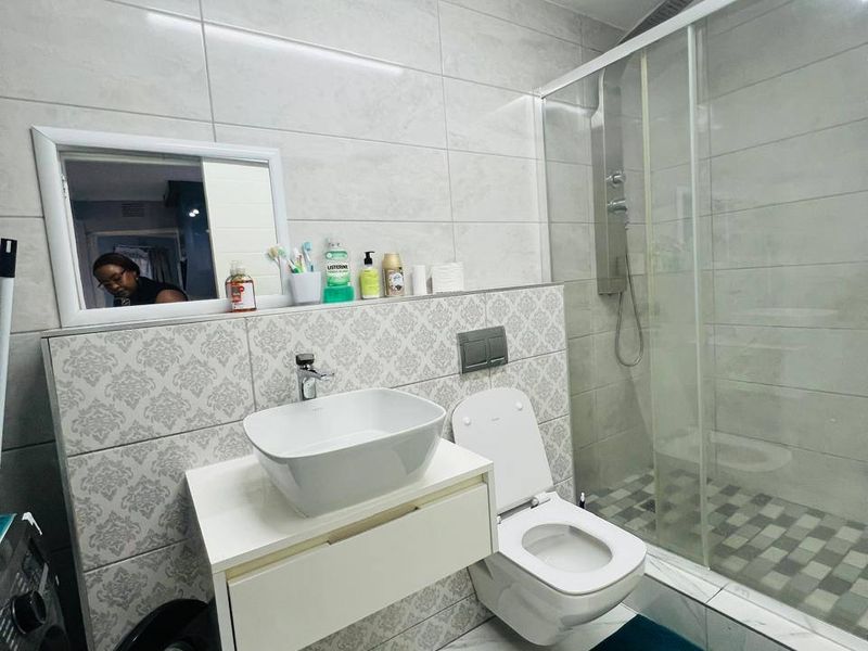 Modern bathroom featuring a wall-mounted vanity with vessel sink, wall-hung toilet with concealed cistern, and a glass-enclosed shower with tiled finishes.