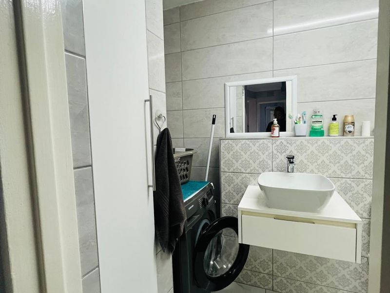 Modern bathroom featuring a floating vanity with a vessel sink, tiled walls and flooring, and a built-in storage cupboard.