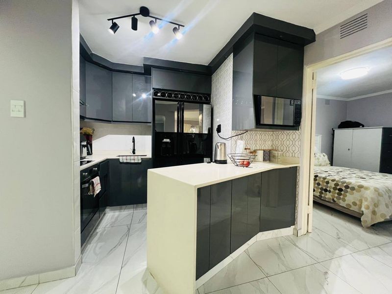 Modern kitchen featuring sleek dark cabinetry, stone countertops, integrated appliances, and contemporary track lighting, with polished tiled flooring throughout.