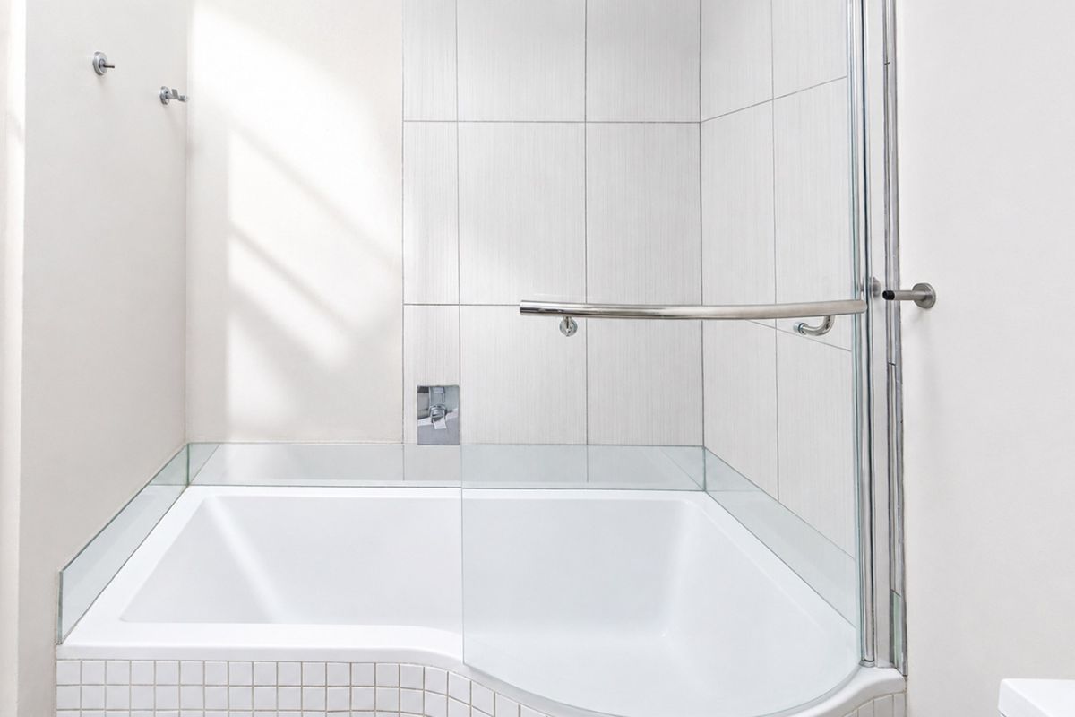 A clean, modern bathroom featuring a built-in bathtub with a glass shower screen, chrome fixtures, and neutral tiled finishes.