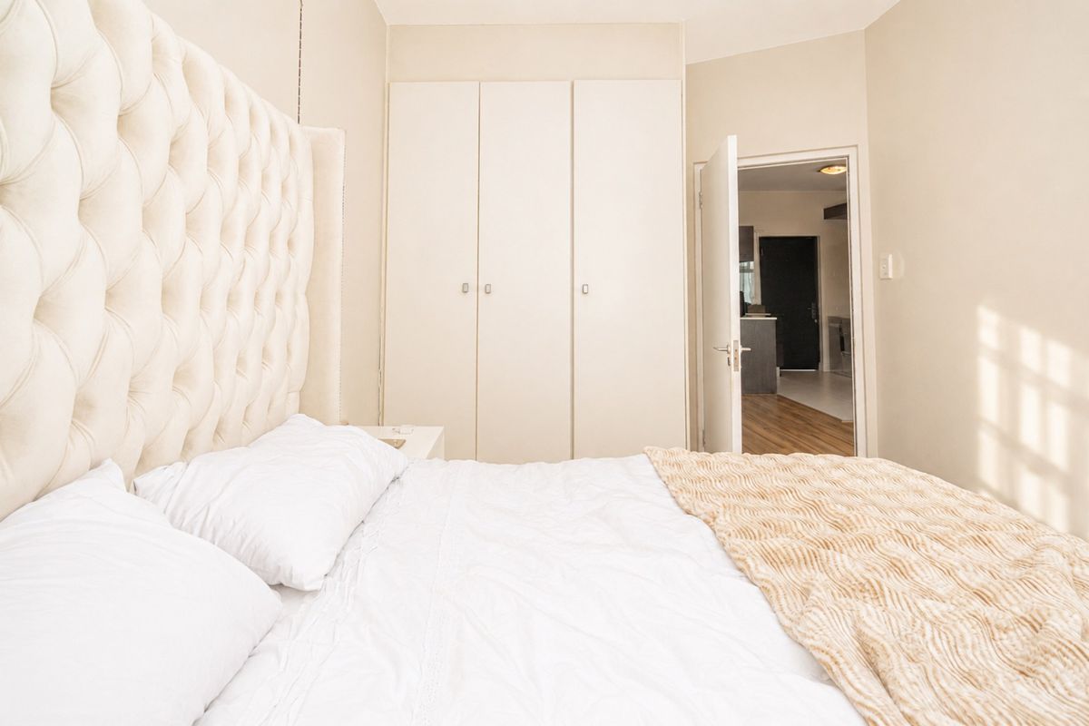 A well-maintained bedroom featuring neutral tones, built-in wardrobe storage, and direct access to the adjoining living area.