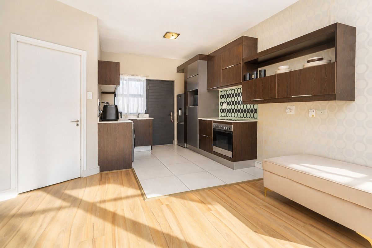 A functional kitchen featuring dark wood cabinetry, a patterned tile backsplash, integrated oven and hob, and a combination of tiled and laminate flooring.