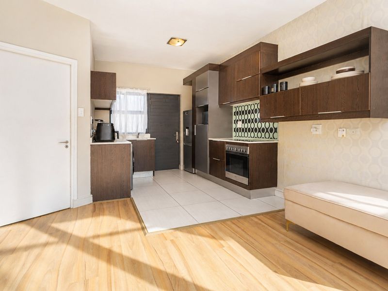 A functional kitchen featuring dark wood cabinetry, a patterned tile backsplash, integrated oven and hob, and a combination of tiled and laminate flooring.