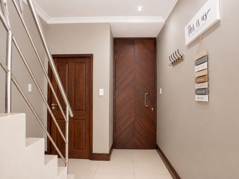 A modern entrance hall featuring a striking chevron-patterned timber front door, tiled flooring, and a sleek stainless steel staircase railing.