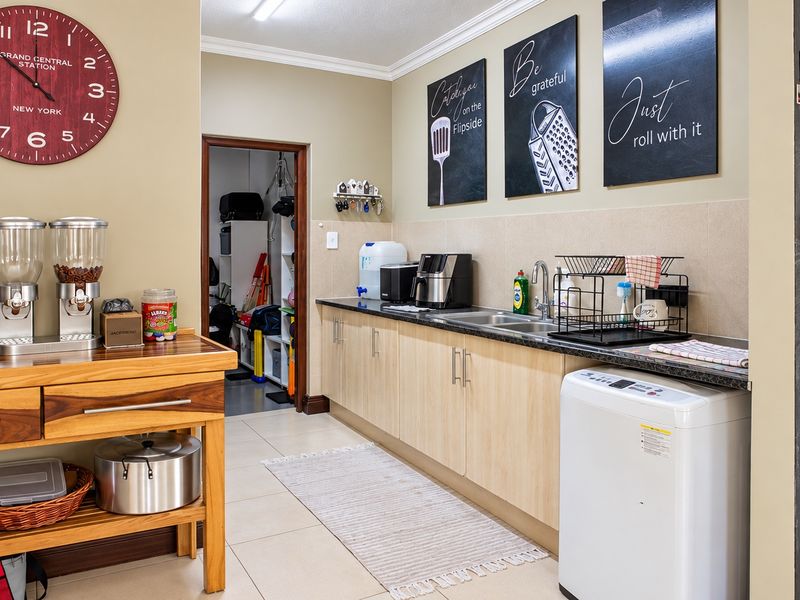 A functional scullery area featuring built-in cabinetry, laminate countertops, a stainless steel sink, and tiled flooring, with an adjacent storage space.