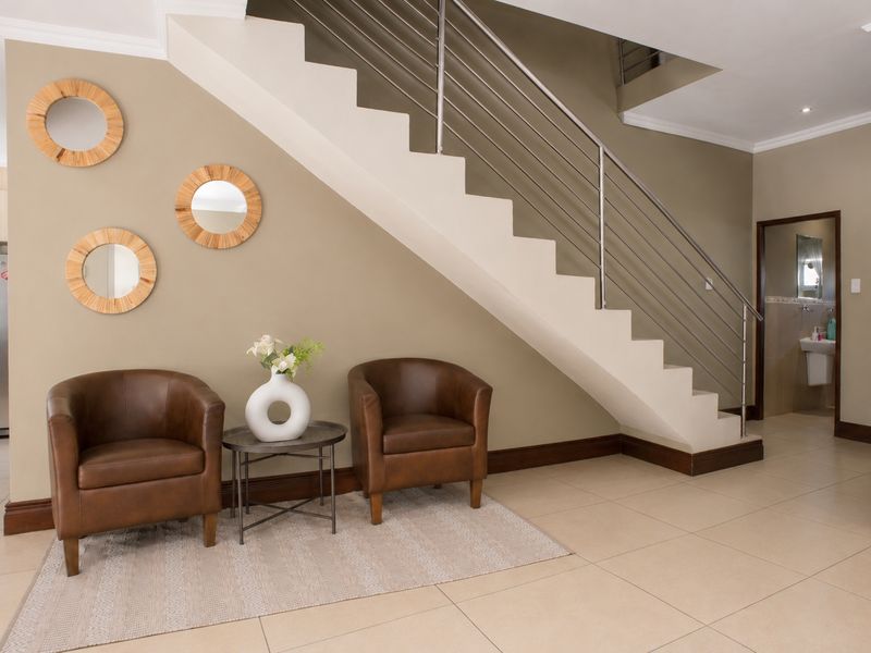 Welcoming entrance area featuring a modern staircase with stainless steel balustrades, neutral wall tones, and clean tiled flooring.