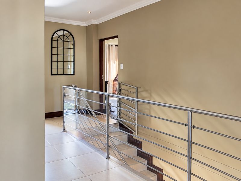 A bright and well-maintained hallway featuring modern stainless steel balustrading, tiled flooring, and an elegant arched window detail.