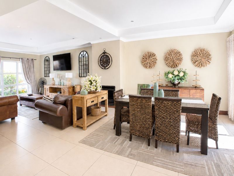 Spacious open-plan living and dining area featuring neutral tiled flooring, recessed ceiling lighting, and a built-in fireplace with access to outdoor space.