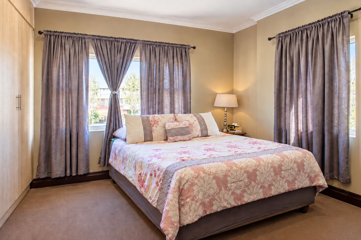 A well-maintained bedroom featuring neutral wall tones, carpeted flooring, and ample built-in cupboard storage with natural light from dual windows.