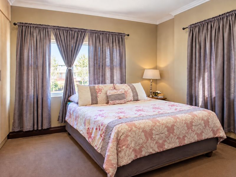 A well-maintained bedroom featuring neutral wall tones, carpeted flooring, and ample built-in cupboard storage with natural light from dual windows.