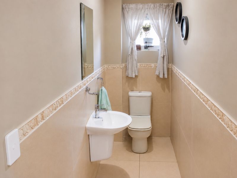 A compact guest bathroom featuring a wall-mounted basin, toilet, and neutral tiled finishes with a decorative border.