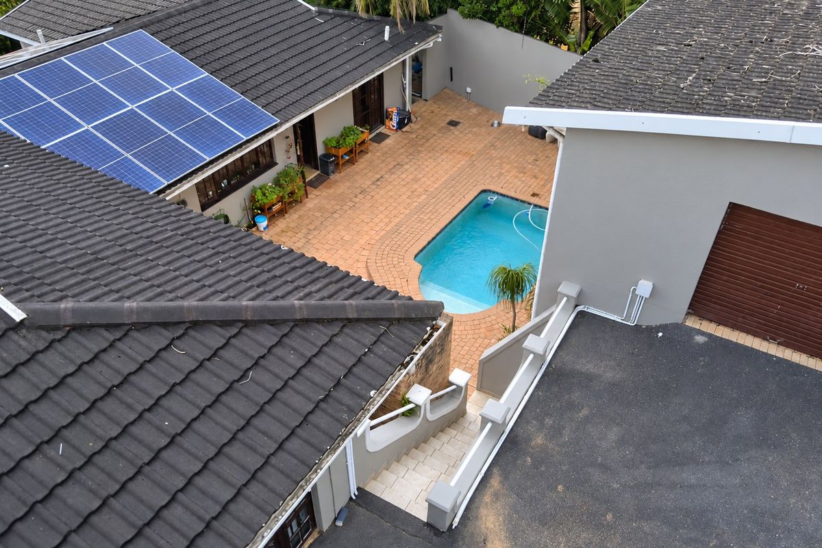 Aerial view of the property featuring a swimming pool, paved courtyard, solar panels on the roof, and a garage with a driveway.