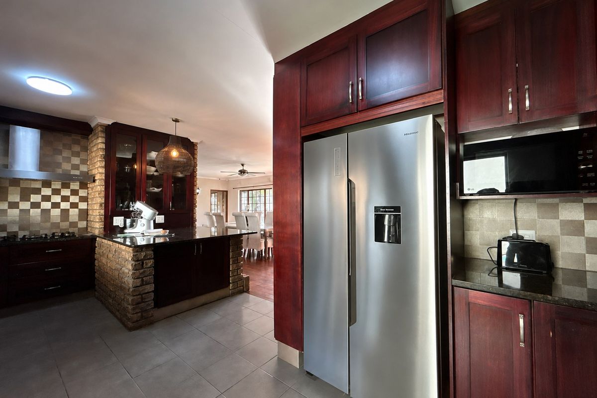 A well-appointed kitchen featuring dark wood cabinetry, granite countertops, a brick feature wall, and integrated appliances, flowing into an open-plan dining area.