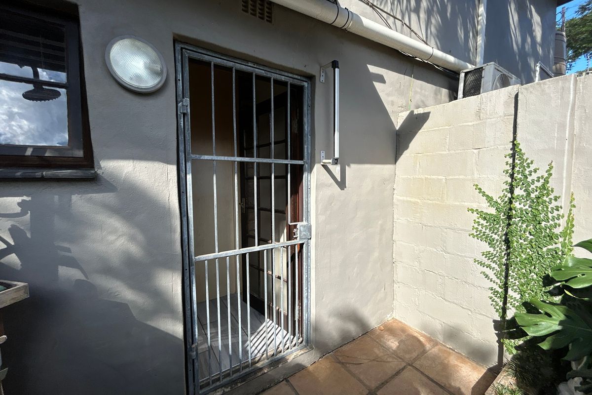 Rear exterior area featuring a security gate, tiled patio flooring, and an external wall-mounted air conditioning unit.