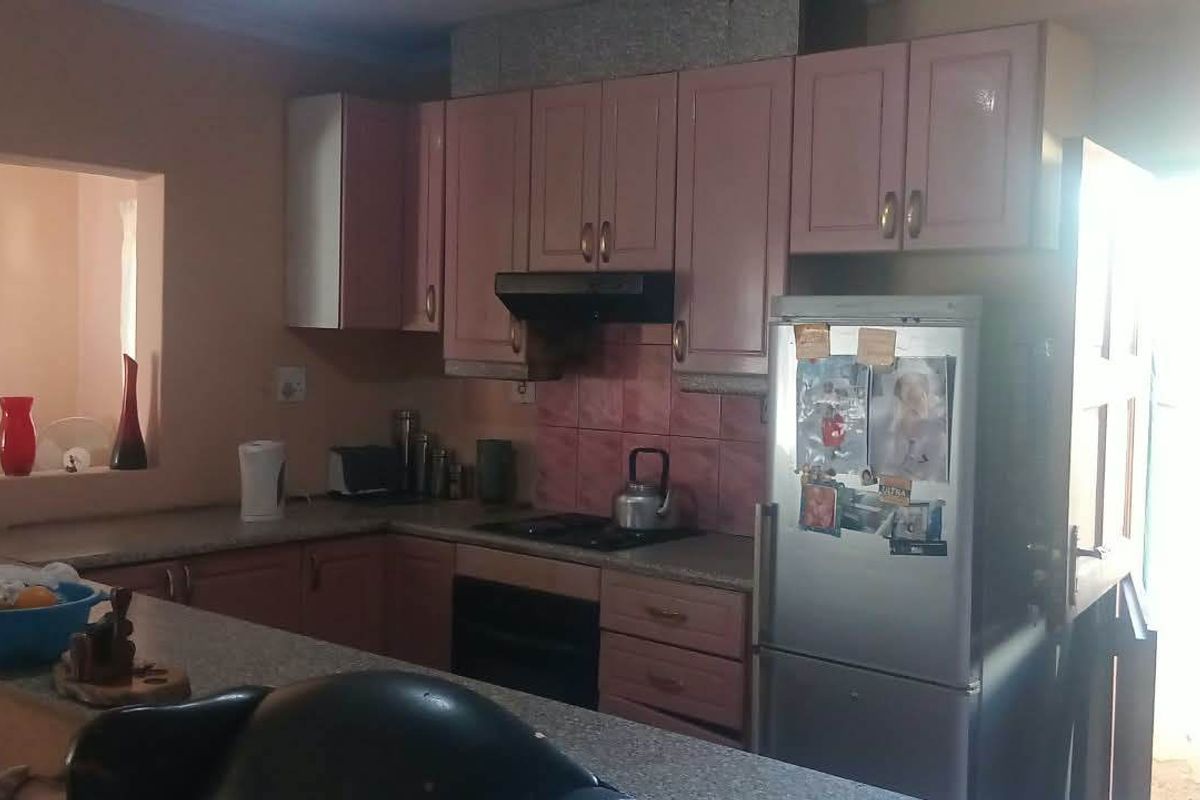 A functional kitchen featuring pink cabinetry, a breakfast bar, and a tiled backsplash, offering a practical layout with direct access to adjacent living spaces.