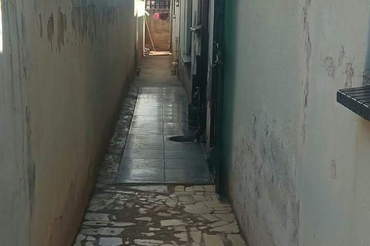 A narrow side passage featuring stone paving and a tiled walkway, bordered by high boundary walls with visible signs of weathering and plaster damage.