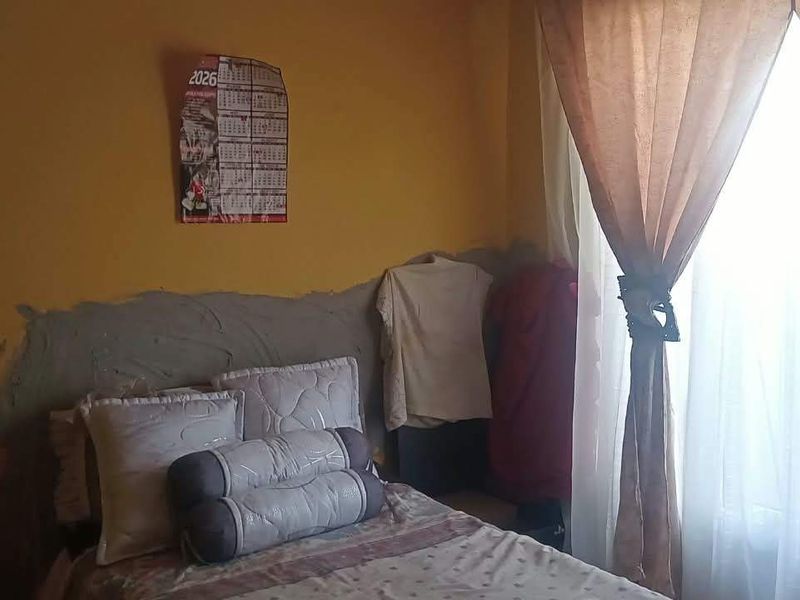 A bedroom featuring a window with curtains and unfinished wall plastering behind the bed area.