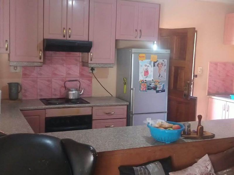 A functional kitchen featuring pink cabinetry, laminate countertops, a breakfast bar, and integrated cooking appliances, offering potential for a modern cosmetic update.