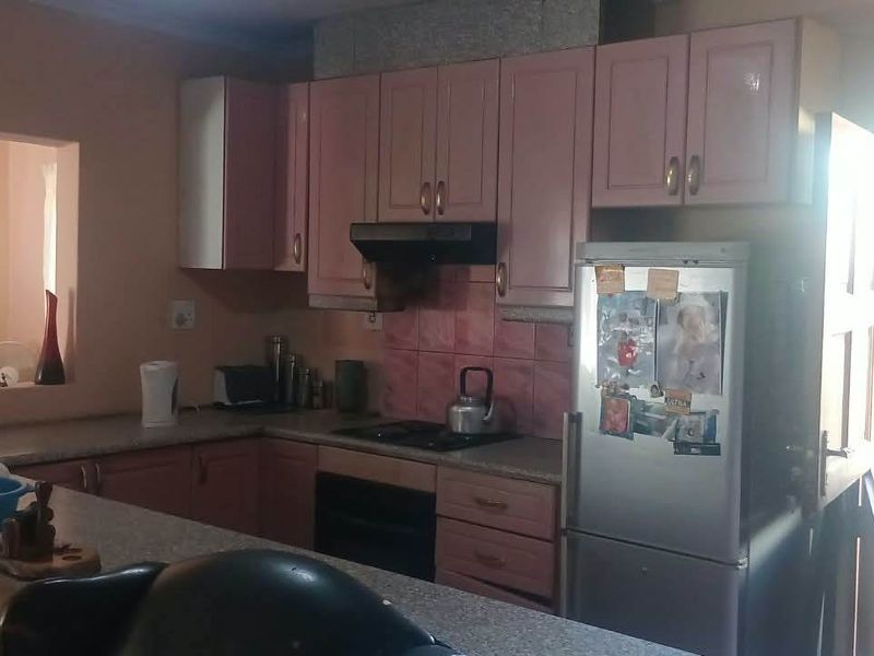 A functional kitchen featuring pink cabinetry, a breakfast bar, and a tiled backsplash, offering a practical layout with direct access to adjacent living spaces.
