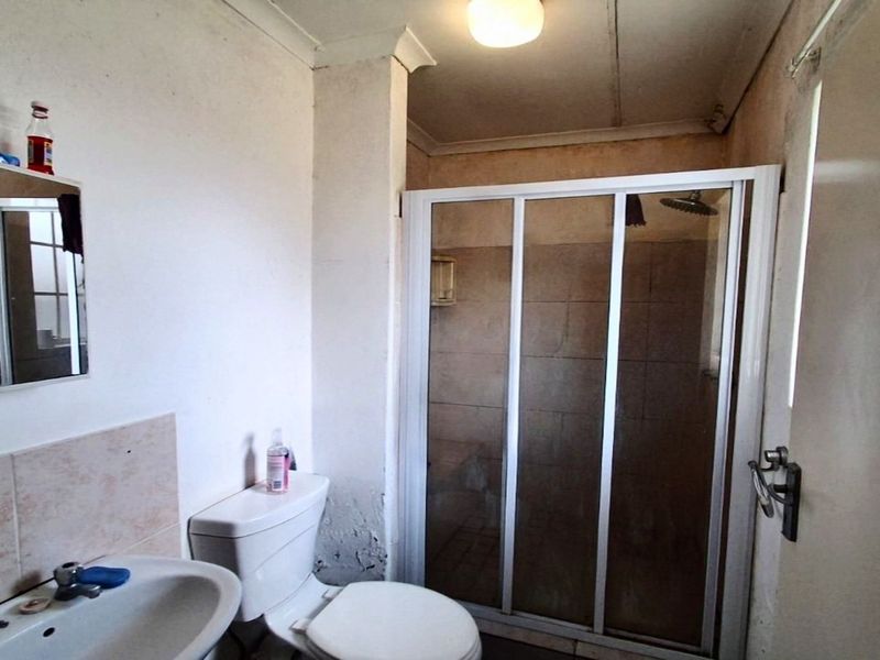 A functional bathroom featuring a shower enclosure, toilet, and washbasin, currently requiring cosmetic updates and repairs to the wall finishes.
