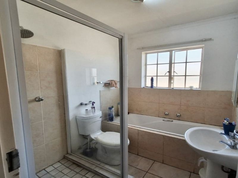 A functional bathroom featuring a shower enclosure, bathtub, pedestal basin, and toilet with neutral wall and floor tiling.