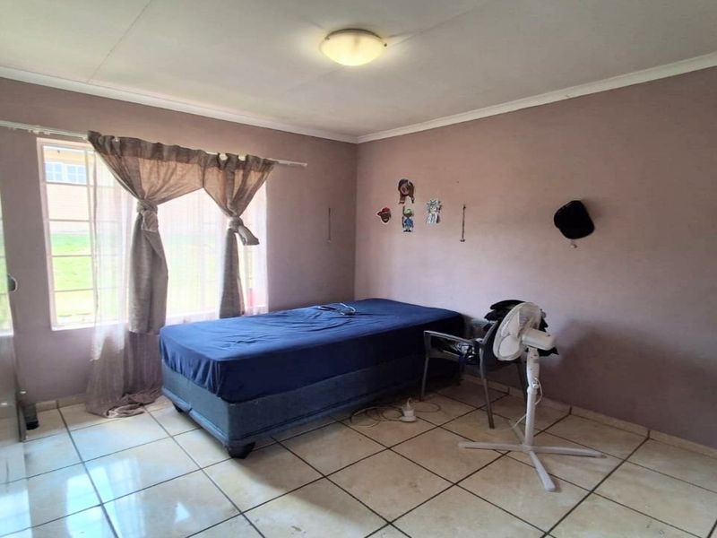 A bedroom featuring tiled flooring and a window, requiring cosmetic updates to the wall finishes to improve the overall aesthetic.
