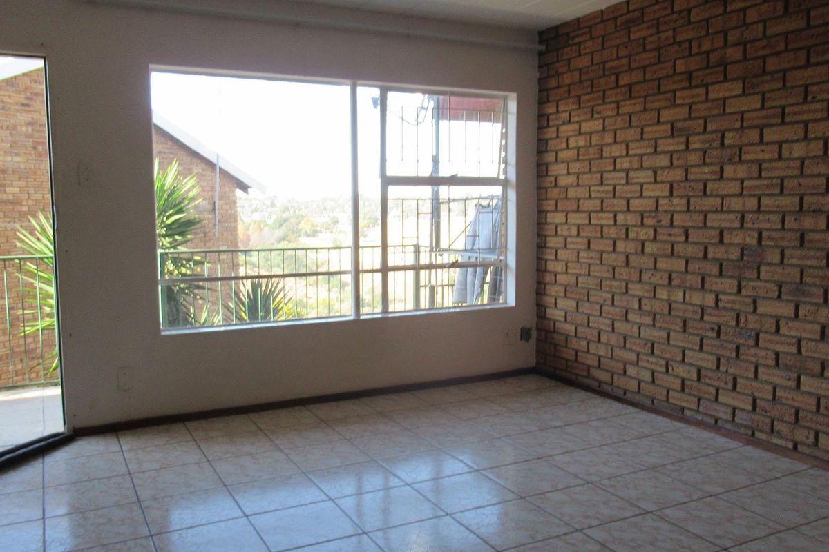 An empty living room featuring an exposed brick wall, tiled flooring, and a sliding glass door leading to a balcony with exterior views.