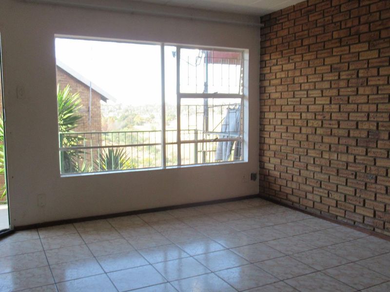 An empty living room featuring an exposed brick wall, tiled flooring, and a sliding glass door leading to a balcony with exterior views.