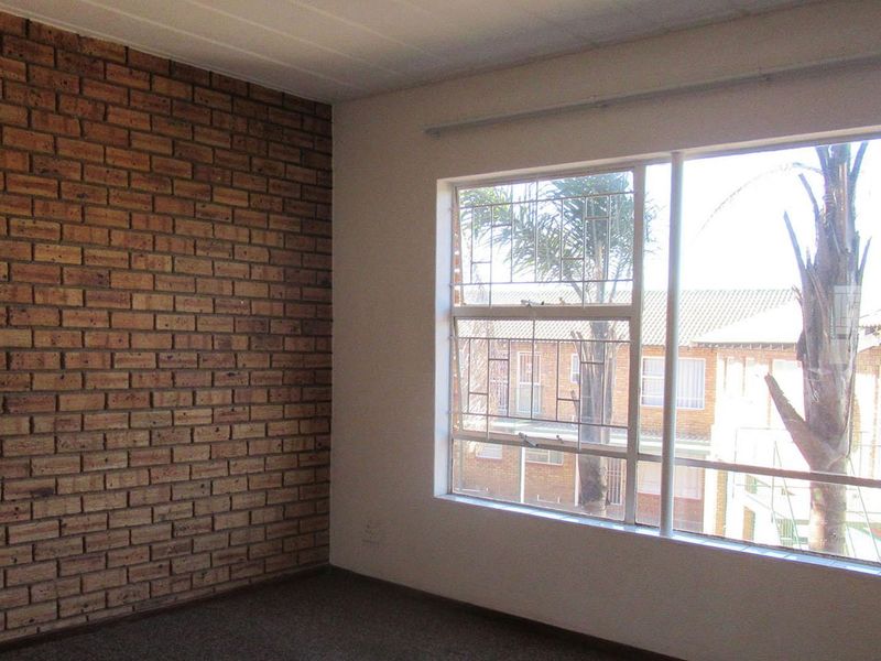 An empty bedroom featuring an exposed brick accent wall, large window with security bars, and carpeted flooring.