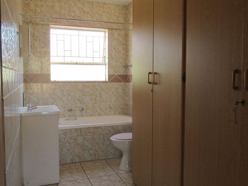 A functional bathroom featuring built-in storage cupboards, a bathtub, a pedestal basin, and a toilet, finished with neutral wall and floor tiling.