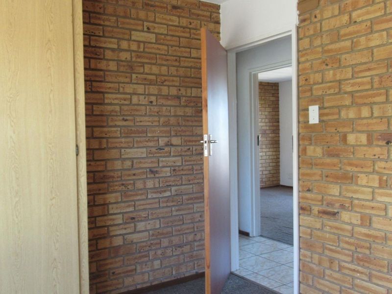 A bedroom featuring exposed brick walls, built-in cupboards, and carpeted flooring, with a doorway leading to an adjacent room.