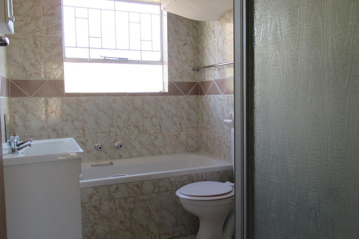 A functional bathroom featuring a built-in bathtub, toilet, and vanity basin with dated wall tiling and a shower enclosure.