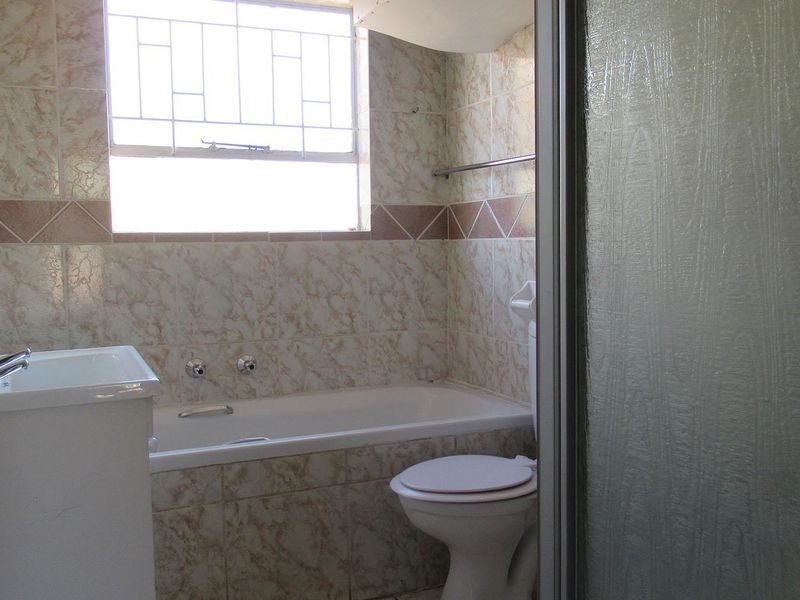 A functional bathroom featuring a built-in bathtub, toilet, and vanity basin with dated wall tiling and a shower enclosure.