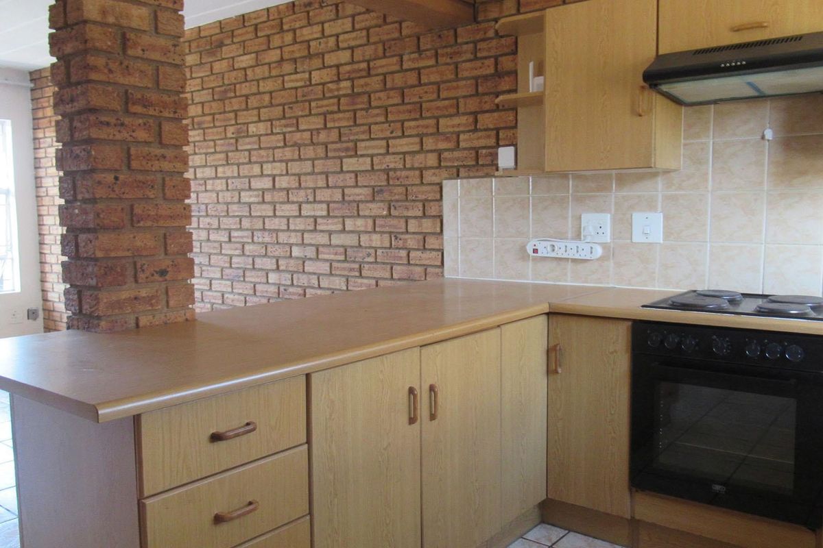 A functional kitchen featuring laminate cabinetry, built-in oven, electric hob, extractor fan, and a distinctive exposed brick feature wall.