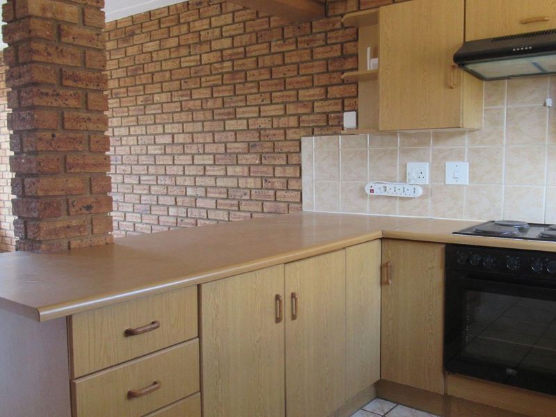 A functional kitchen featuring laminate cabinetry, built-in oven, electric hob, extractor fan, and a distinctive exposed brick feature wall.