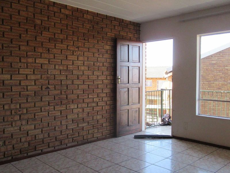 An empty living room featuring an exposed brick wall, ceramic tiled flooring, and direct access to an outdoor balcony area.