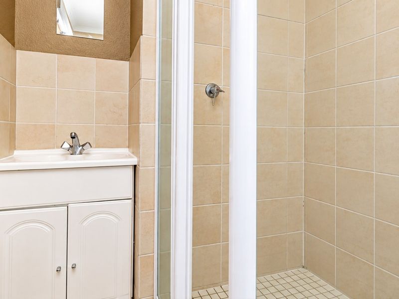 A compact bathroom featuring a vanity cabinet with a basin, chrome mixer tap, and a tiled shower enclosure.